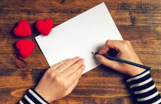 Mani che scrivono su un biglietto, accanto dei cuoricini cosa scrivere san valentino, idee san valentino